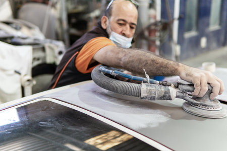 Auto mechanic sanding a part of a car in a garage. Preparing for painting the car in a workshop....