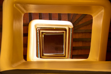 The view into the rectangular central part of a staircase, which is bathed in warm light and where...