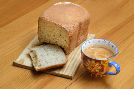 cup with coffee and homemade bread with a slice cut on wooden board