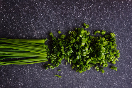 finely chopped green fresh chives lie on a black marble cutting boardの写真素材