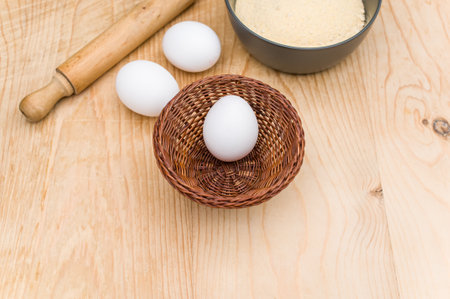 white eggs and dark gray bowl with whole grain flour and rolling pin on worn wooden background with copy spaceの写真素材