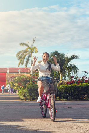 A happy young latin girl is riding a bicycle without hands in the parkの写真素材