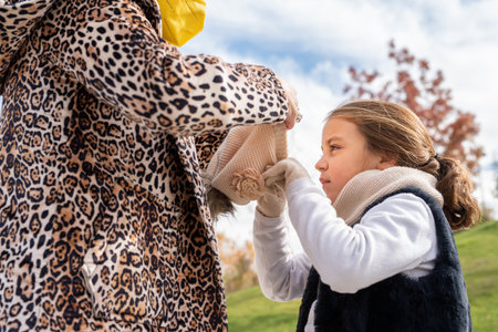 Caucasian girl helped by her mother putting on a winter hat on a cold day.の写真素材