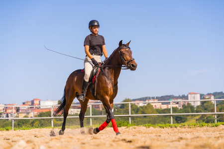 Young Caucasian blonde girl riding on a horse with a brown horse, dressed in black rider with safety...