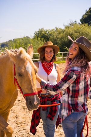 Two cowgirl women caressing a horse on a horse riding, with South American outfits, the two young women posingの写真素材