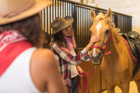 Two cowgirl women stroking a horse, with South American outfits, lifestyle of two working in a stableの写真素材