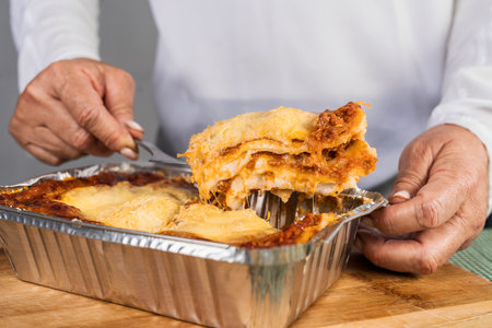 Close up view of an adult woman taking out a portion of freshly made lasagna with bolognese ready to eat.の写真素材