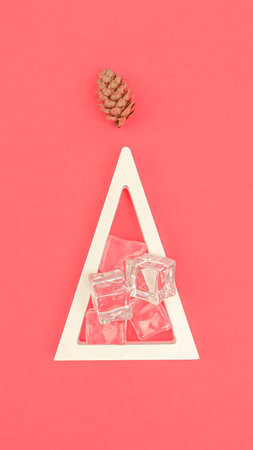 Abstract Christmas concept. A modern form of the Christmas tree. White wooden triangle filled with cold ice cubes. Coral background. Geometry and straight lines. The simplicity of NY composition.の写真素材