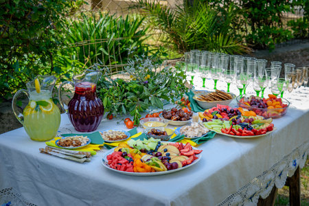 Decorated table served outdoors with fruits, drinks, food, crockery and glasses