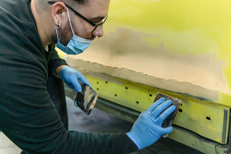 Auto mechanic repairing a yellow car with putty for paint in a workshopの写真素材