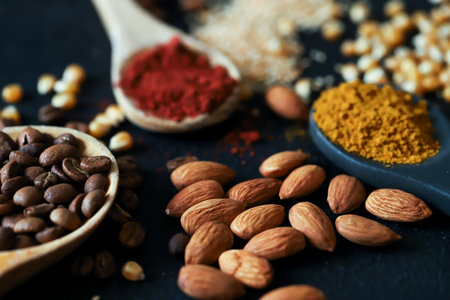 different spoons filled with spices and grains, you will find nuts, curry, paprika, coffee, corn, sunflower seeds on a black background.の写真素材