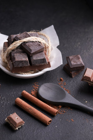 rustic stick spoon with powdered and bar chocolate on a dark background