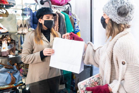 Employee with masks in a clothing store handing over clothes to a customer, security measures in the coronavirus pandemic, covid-19の写真素材