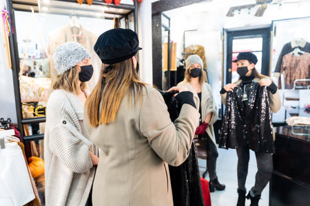 Caucasian employee of a luxury clothing store showing a sequin dress in front of a mirror, security measures in the coronavirus pandemic, covid-19の写真素材