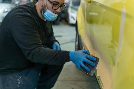 Auto mechanic repairing a yellow car with putty for paint in a workshop