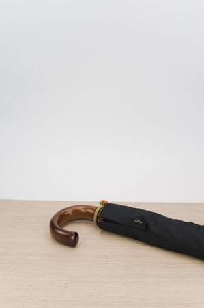 black foldable umbrella with solid wood handle on a wooden surface with copy spaceの写真素材