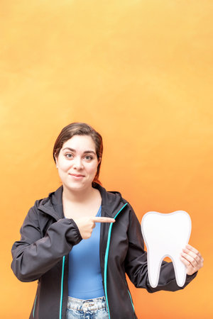 Girl pointing to a tooth shape, isolated over orange background.