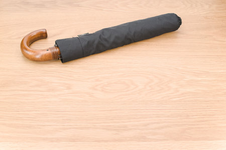 black foldable umbrella with solid wood handle on a wooden surface with copy space