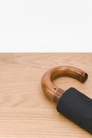 black foldable umbrella with solid wood handle on a wooden surface with copy spaceの写真素材