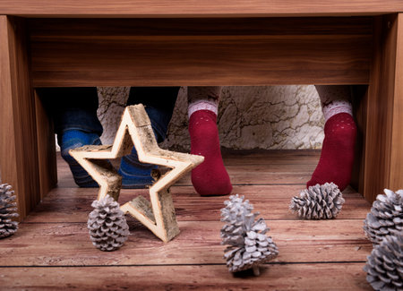 Feet of couple sitting at home on a brown bench wearing wool socks with christmas decoration in frontの写真素材
