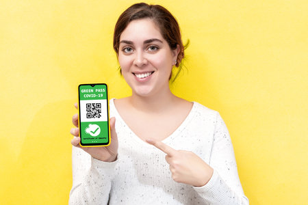Smiling positive young woman shows a digital green pass on smart phone.の写真素材