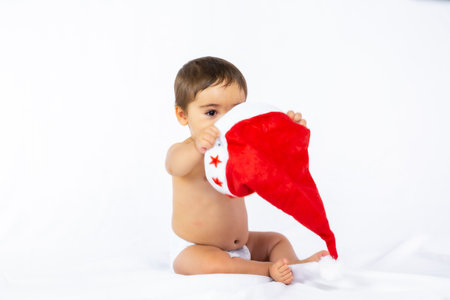 A baby boy with a red Christmas hat on a white background, copy space, playing with Santa's hatの写真素材