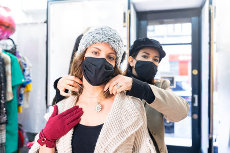 Employee with a mask in a clothing store trying on a client a jewel, working with security measures in the coronavirus pandemic, covid-19の写真素材