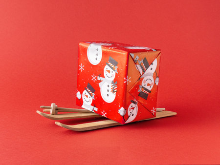 Red Christmas gift on Santas wooden skies, against red background. Minimal nature composition....