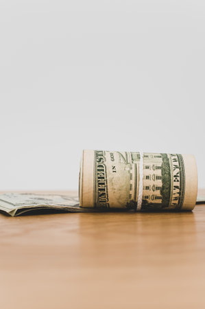 US dollar banknotes rolled up on a wooden tabletop with text spaceの写真素材