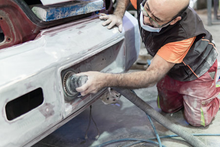 Auto mechanic sanding a part of a car in a garage. Preparing for painting the car in a workshop