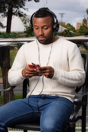 Afro-descendant attractive latin Colombian man listening to music on his cell phone with headphones...