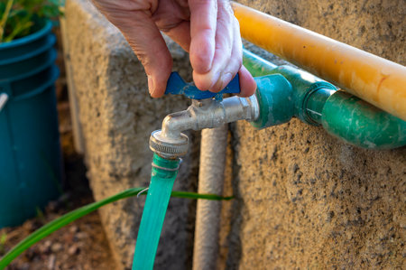A person's hand closing a water tap with a piece of hose connected to its outlet