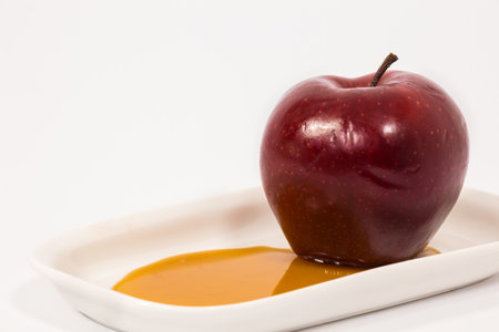 Red apple on white plate with honey isolated on a white background. Symbols of Jewish New Year - Rosh Hashanah.の写真素材