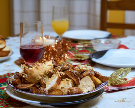 Christmas table with plate in the foreground with chicken and rustic potatoes, glass of wine and Christmas decorationsの写真素材