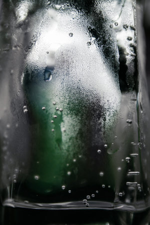Texture water drops on glass of water that look like ice block.Green bottle appears blurred in the...