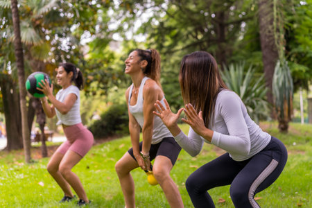 Latin girl doing sports in a green park, lifestyle a healthy life, teacher with the students doing squats with the weight ballの写真素材