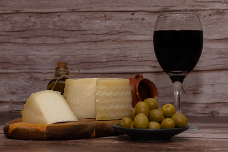 cured cheese cut with a glass of red wine, stuffed olives and extra virgin olive oil on a wooden table copy-spaceの写真素材
