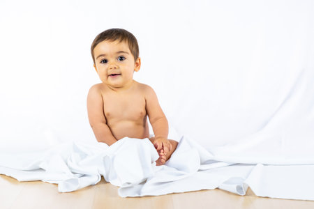 Baby boy in a studio with a white background, eight month old Caucasian newborn sitting, playing with a clothの写真素材