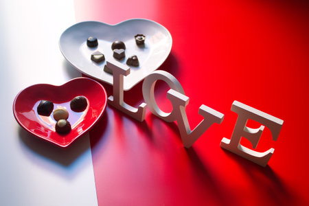 two dishes, one red and one white, in the shape of a heart with chocolate bonbonsの写真素材