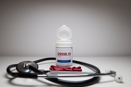 A stethoscope and a white bottle of covid-19 antiviral pills opened and with the pills out of the bottle on the laboratory table. Concept of the new antiretroviral treatment pill Covid-19.の写真素材