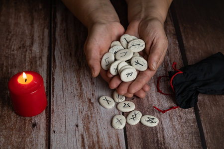 woman's hands teaching rune stones with black symbols for fortune telling on a wooden tableの写真素材