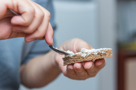 Woman preparing breakfast, putting soft cheese on rye bread. Female hands making a sandwichの写真素材
