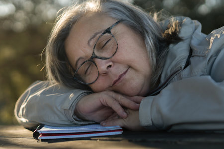 older white-haired woman with glasses asleep on her notebook in the park dreamingの写真素材