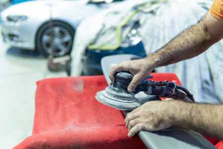 Auto mechanic sanding a part of a car in a garage. Preparing for painting the car in a workshop. Blurry movementの写真素材
