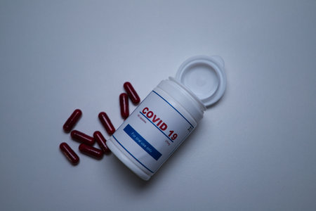 A white covid-19 antiviral pill bottle open and lying with the pills out of the bottle on the...