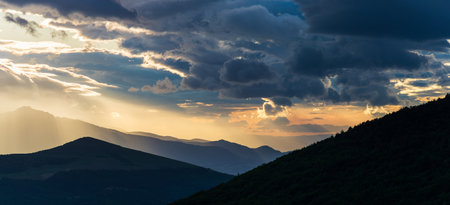 Sunset dramatic sky over epic mountain range silhouette, Marche, Italy. Sunbeams among clouds above...
