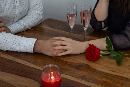 hands of a couple with champagne candles and a red rose on a wooden table