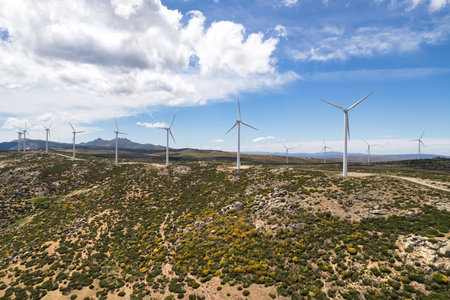 Drone point of view moving turbines of windmills. Wind energy converter into electricity. Panoramic image, cultivated farm lands during sunny summer day on blue cloudy sky background. Europe, Spainの写真素材