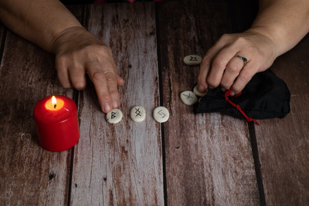 woman's hands teaching rune stones with black symbols for fortune telling on a wooden tableの写真素材