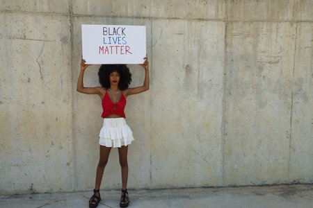 Young, beautiful African-American woman with banner claiming the rights of her community against a...